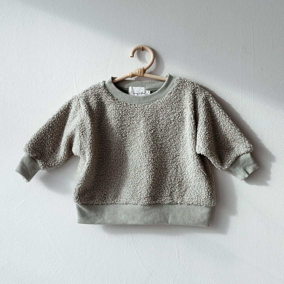 Gray children's sweater on a hanger against a light gray background