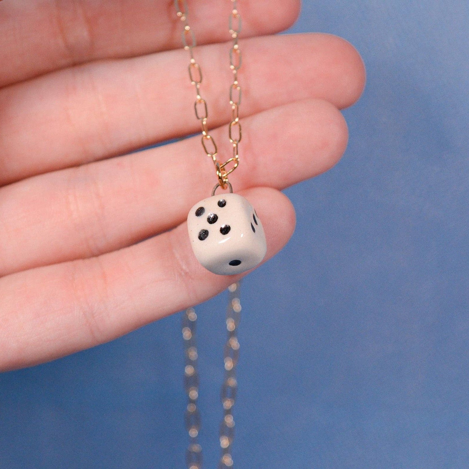 Necklace with a dice pendant held by a hand against a blue background