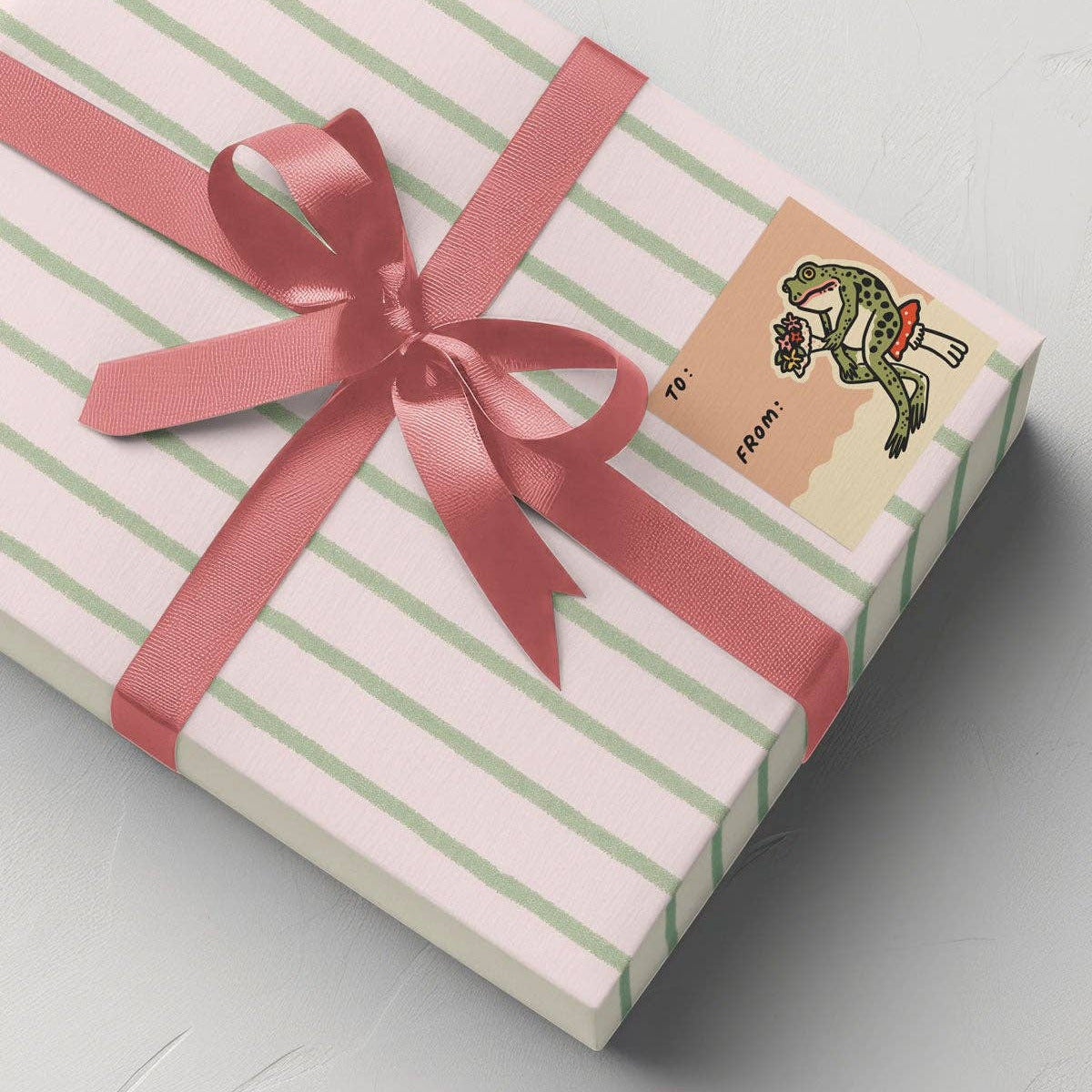 Gift box with pink and green stripes and a pink ribbon on a light gray background
