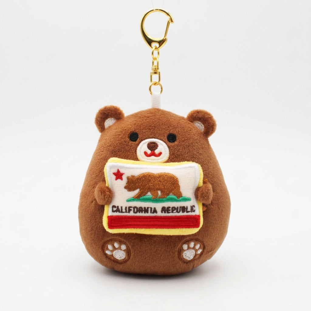 A brown plush bear keychain holding a California Republic flag patch, featuring a gold metal clasp at the top, photographed against a plain white background.