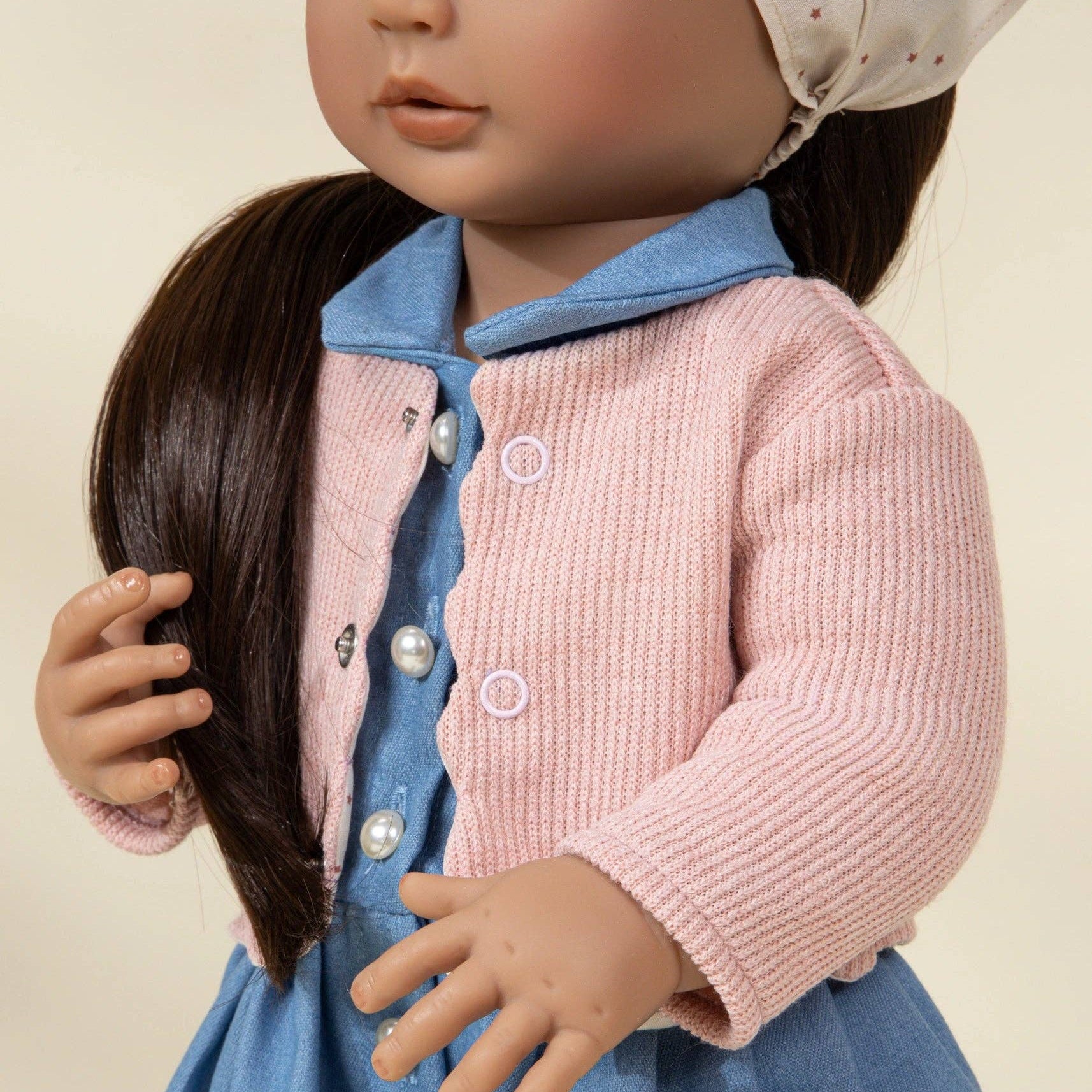 Doll wearing a pink cardigan over a blue dress with a white collar.