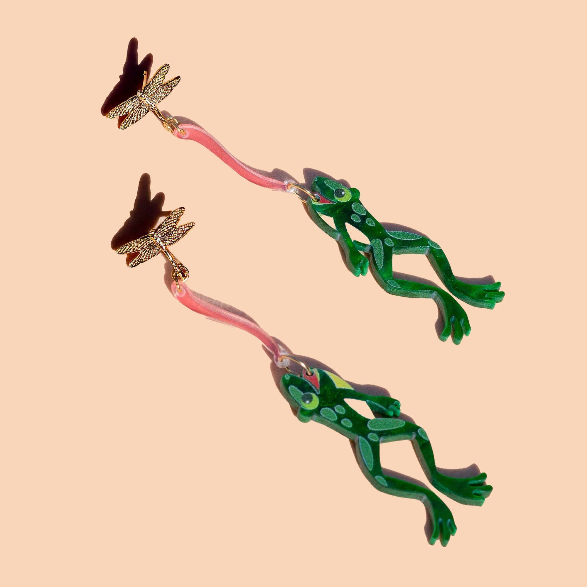 Frog-shaped earrings on a beige background