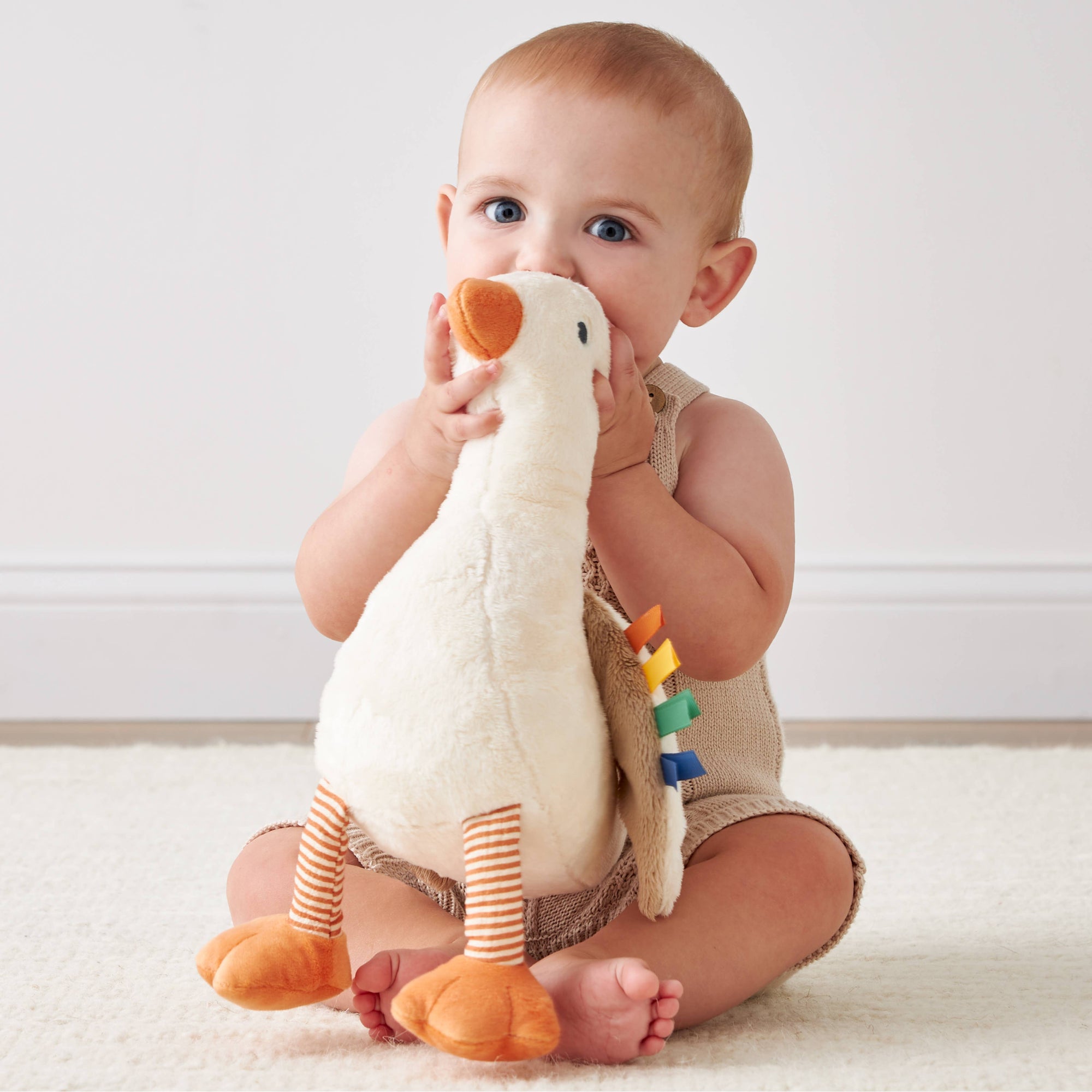 Baby playing with a plush toy duck on a light-colored floor.