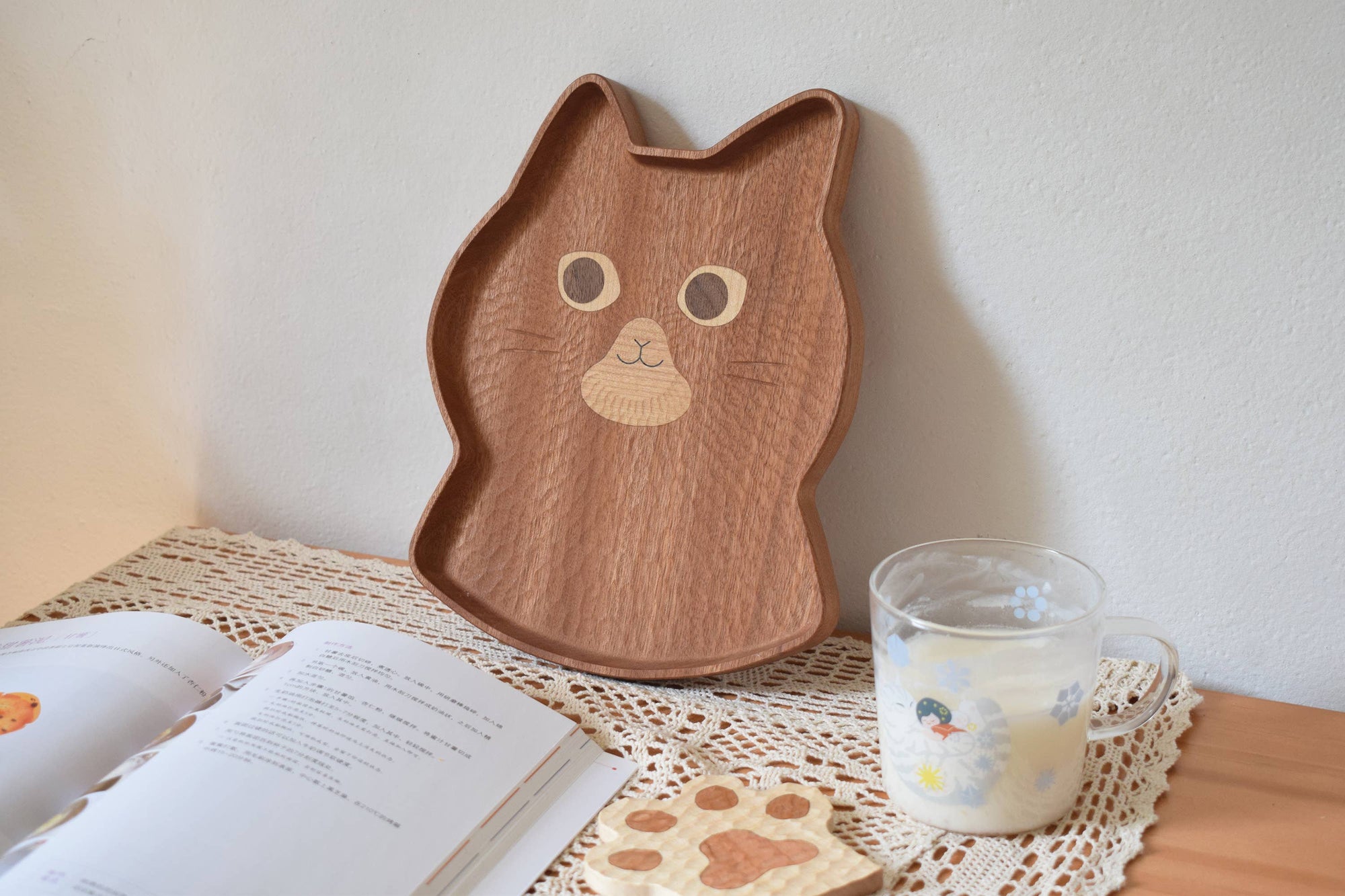 Wooden tray shaped like a cat with a glass of milk and book on a table