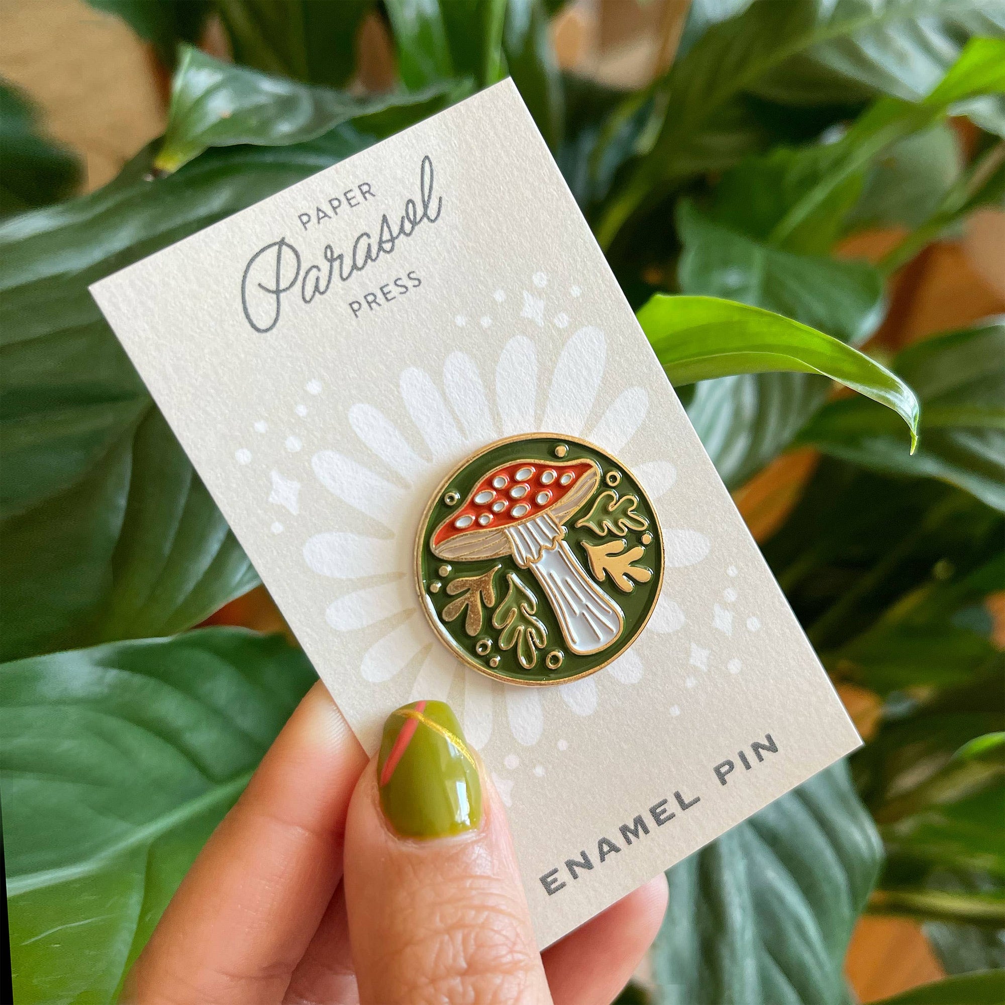 Enamel pin on a Paper Parasol Press card with green leaves in the background