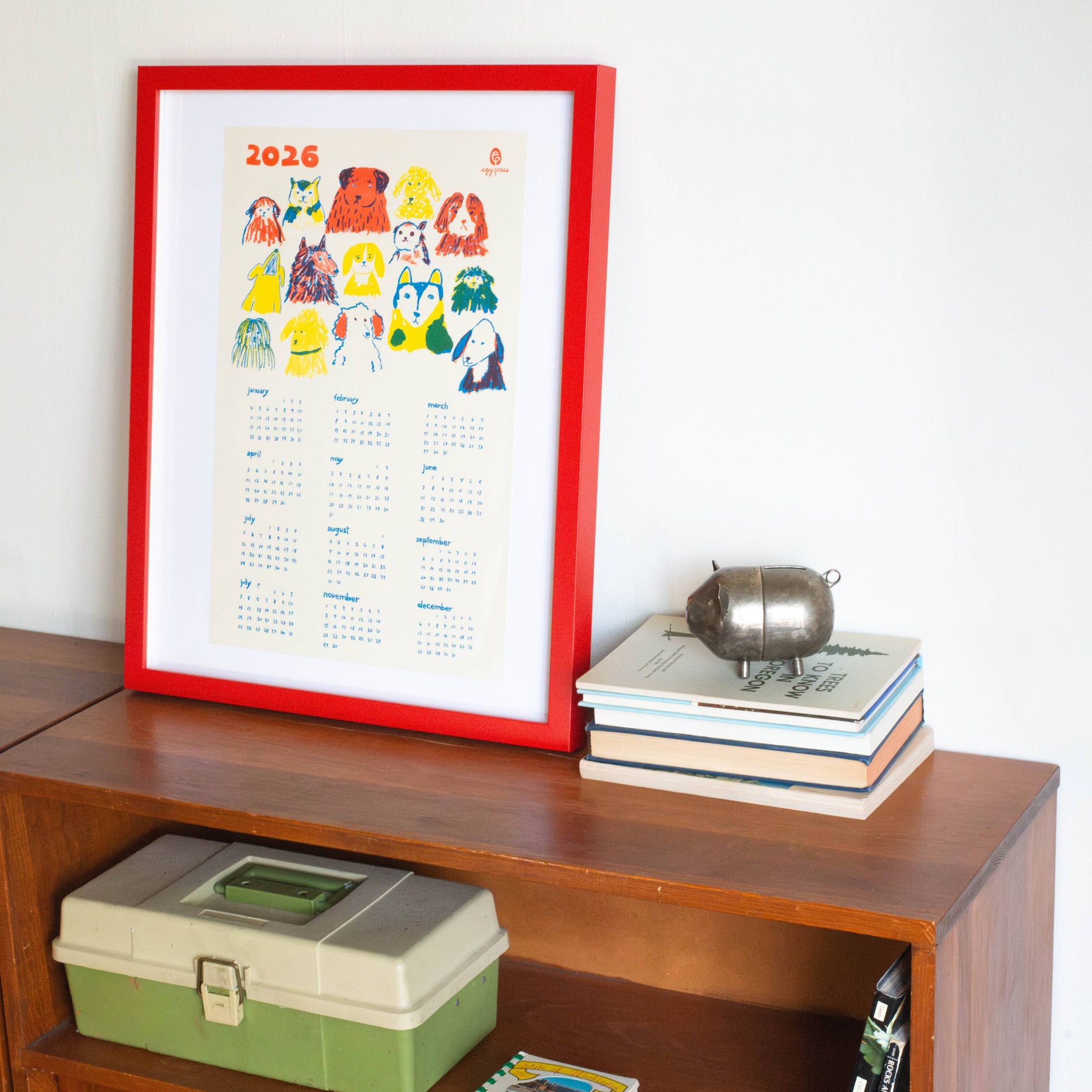 Framed calendar on a wooden shelf with books and a silver pot