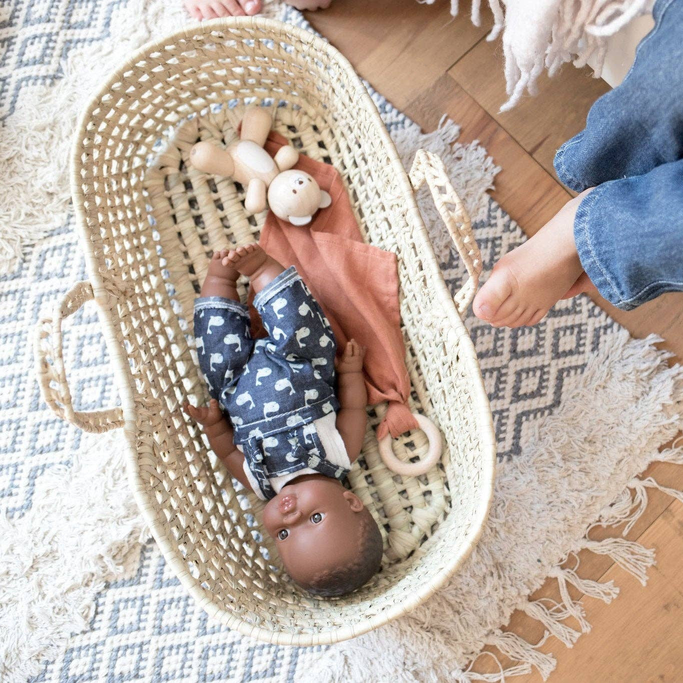 Baby doll in a bassinet with toys on a patterned rug