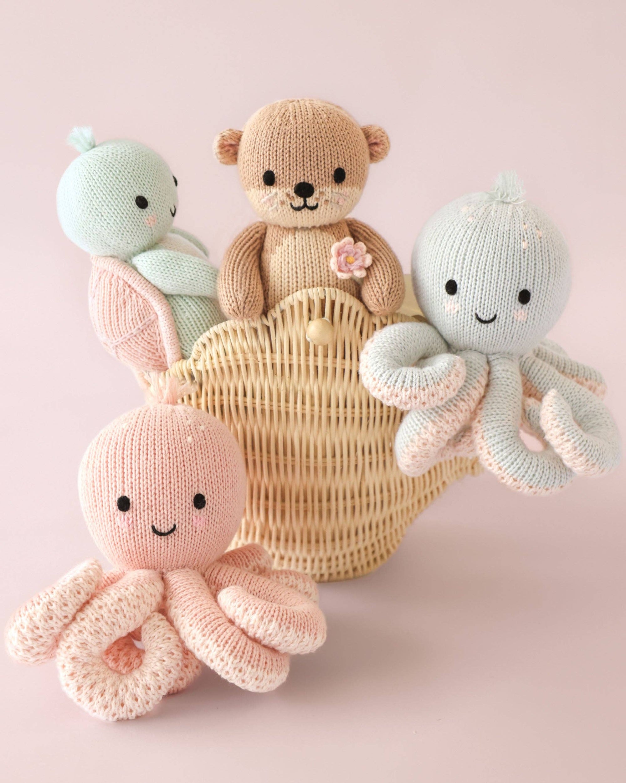 Knitted toys including a bear, octopus, and ball in a basket on a pink background