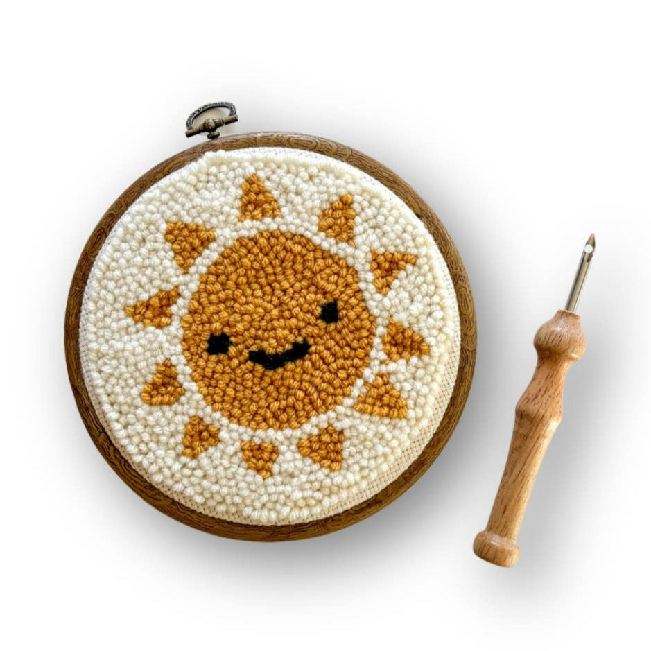 Embroidery hoop with a smiling sun design and a wooden needle on a white background