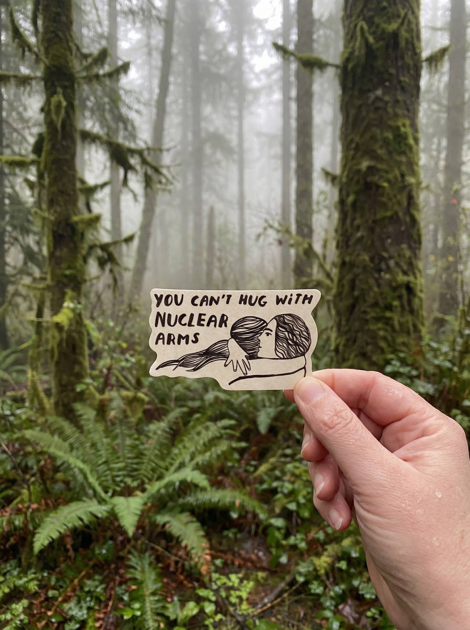 Hand holding a sign with text and illustration in a forest