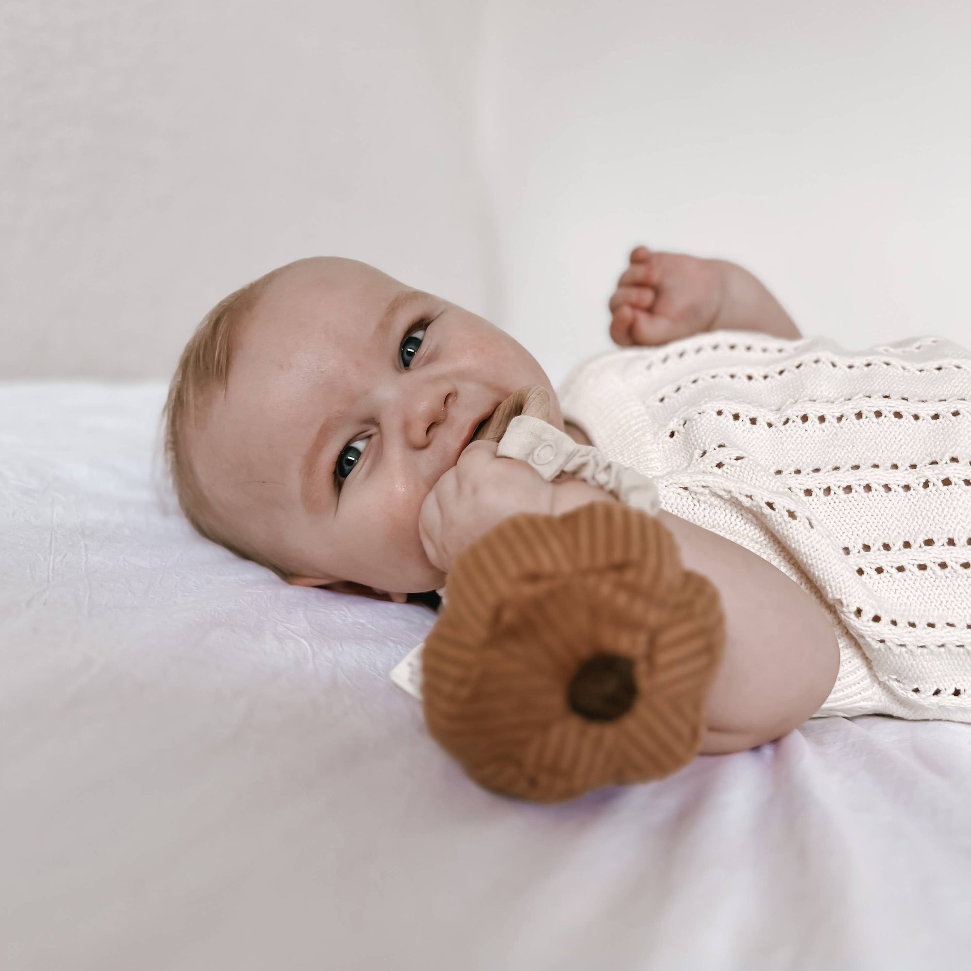 Baby lying on a white surface with a brown knitted toy