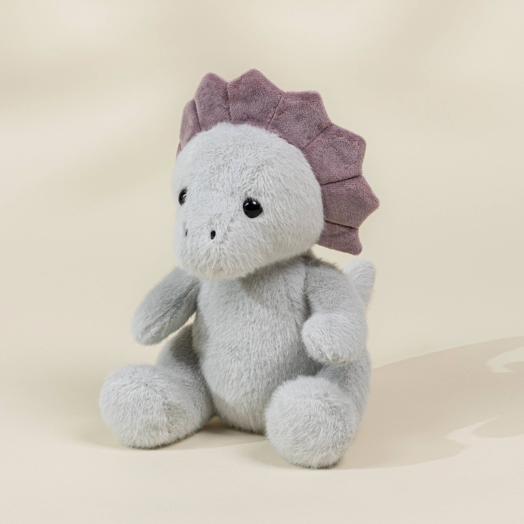 Plush dino toy with a purple fringe on a beige background