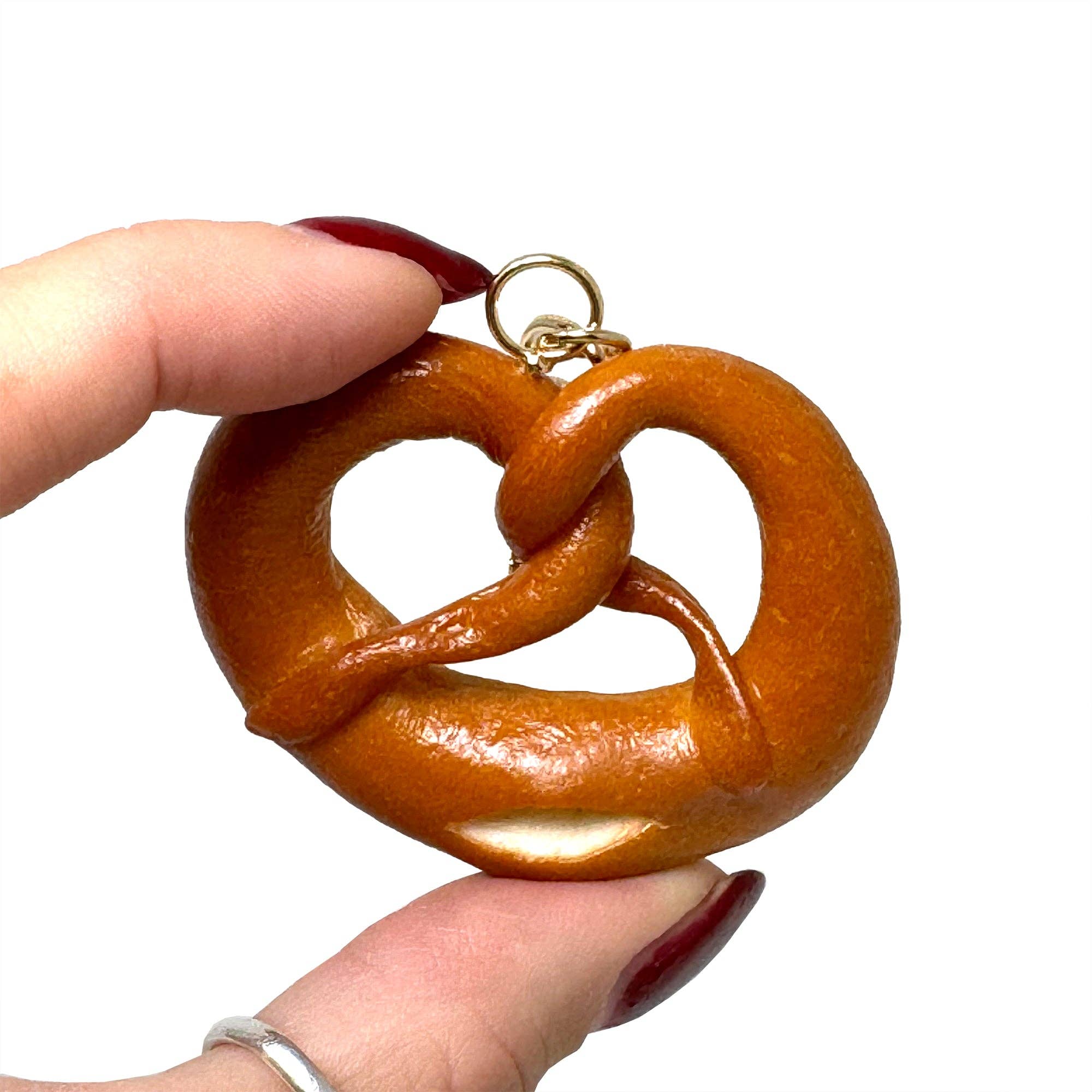 Pretzel-shaped keychain held by a hand with red nail polish on a white background