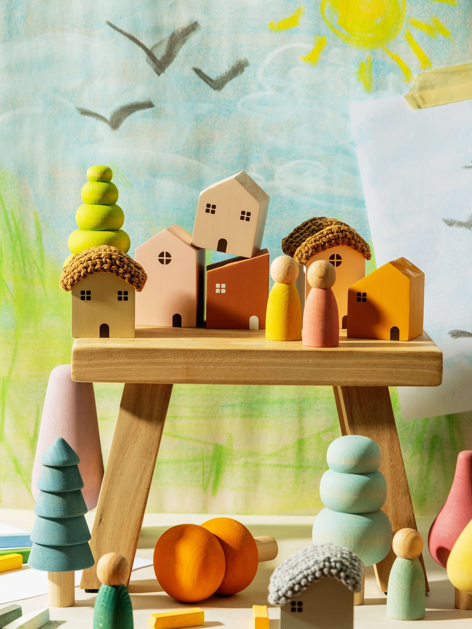 Colorful wooden toys on a stand with a child's drawing of a house and sun in the background.