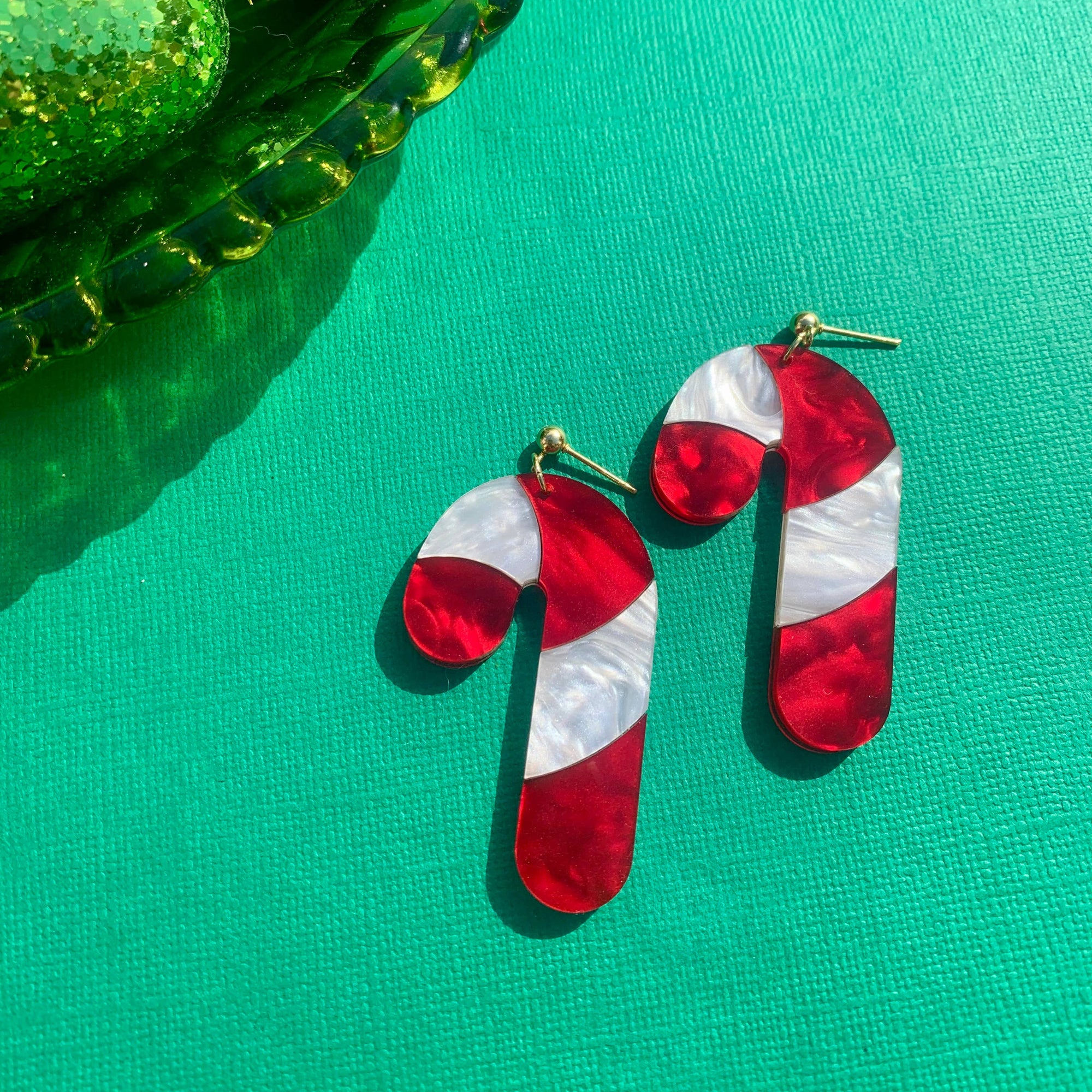 Red and white striped candy cane earrings on a green surface with Christmas ornaments.