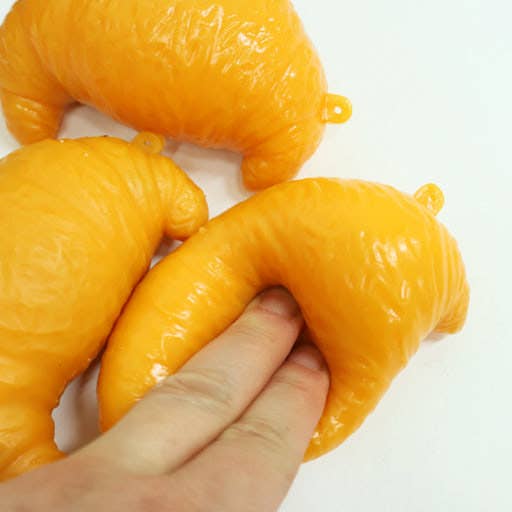 Three glossy, yellow-orange, crescent-shaped squishy toys on a plain white background, with a human hand pressing down on one of them to demonstrate texture and flexibility.
