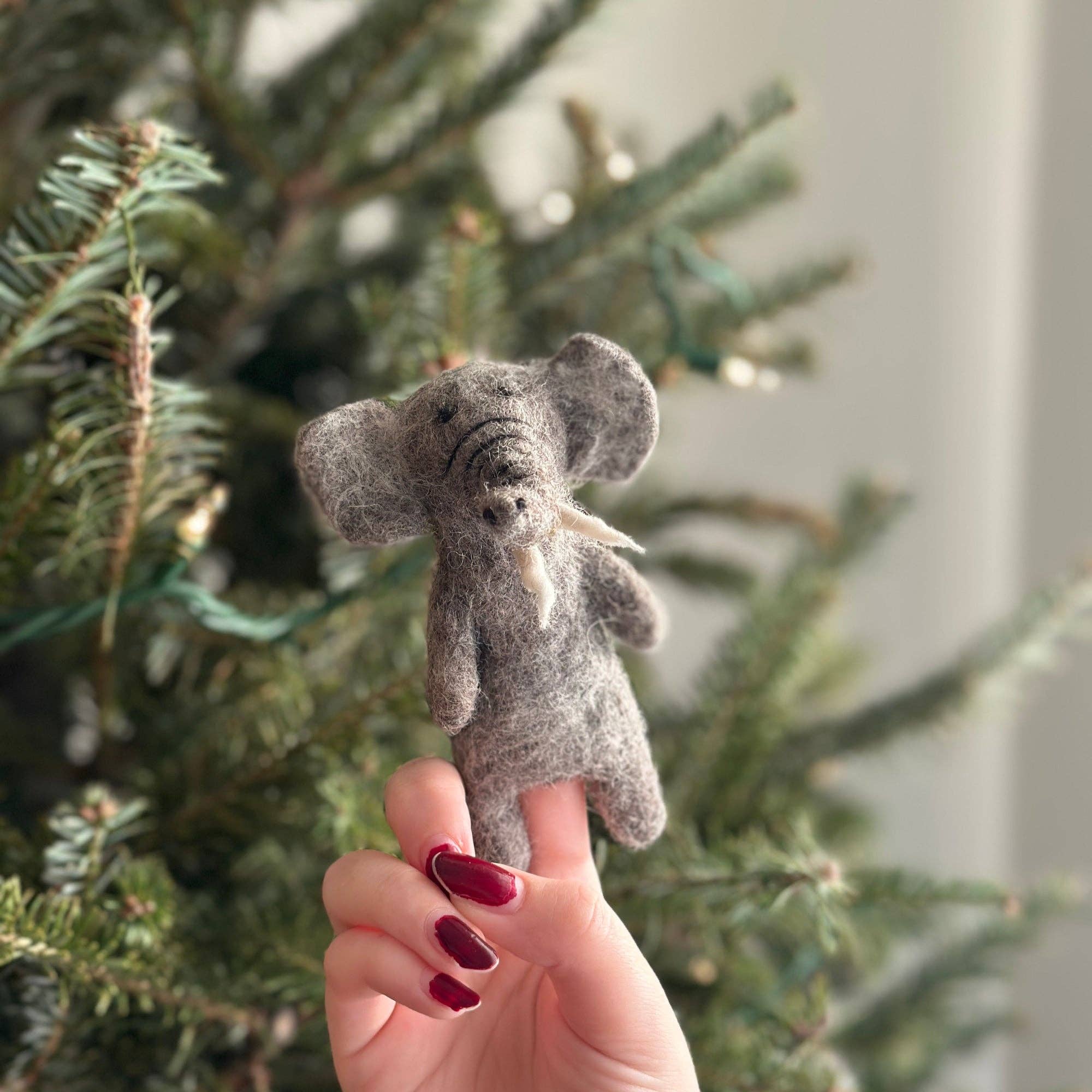 Small gray felt elephant toy held in front of a Christmas tree.