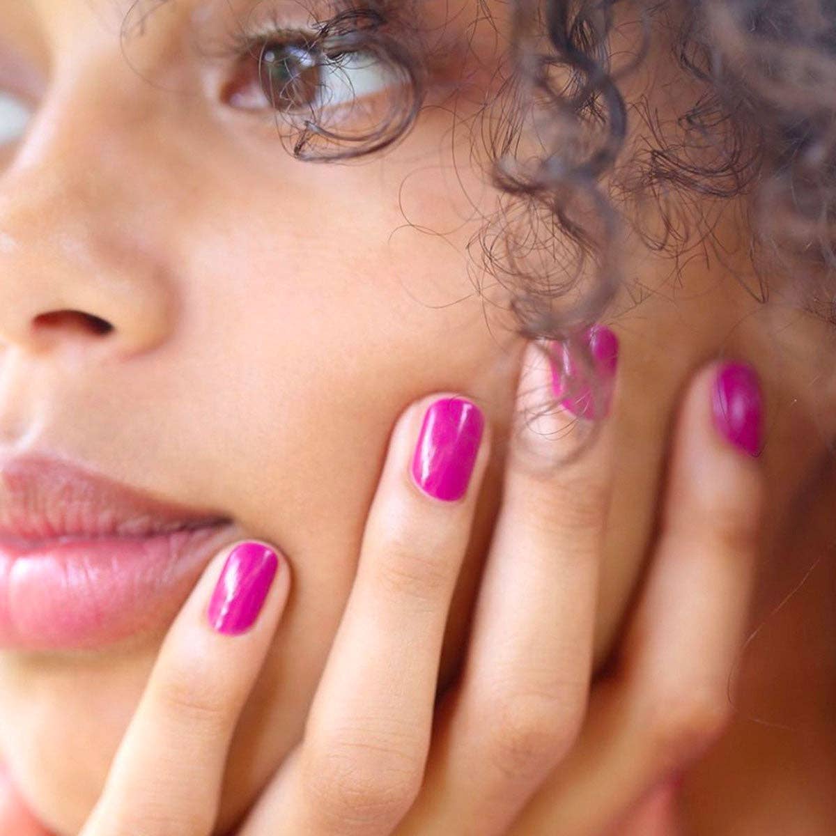 Close-up of a woman with pink nail polish touching her face.