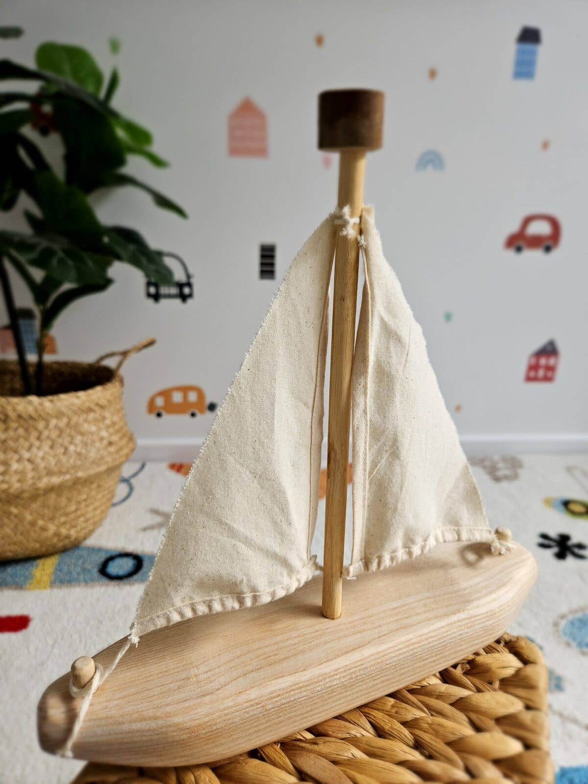 Wooden sailboat model on a textured surface with a colorful wall in the background