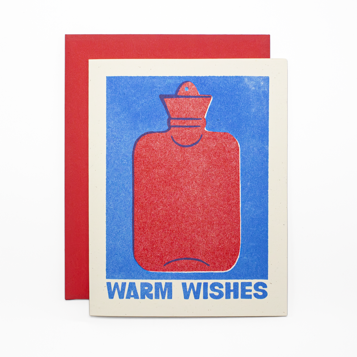 A greeting card with a red hot water bottle illustration on a blue background and the words 'WARM WISHES' in blue, shown with a red envelope behind it on a white background.