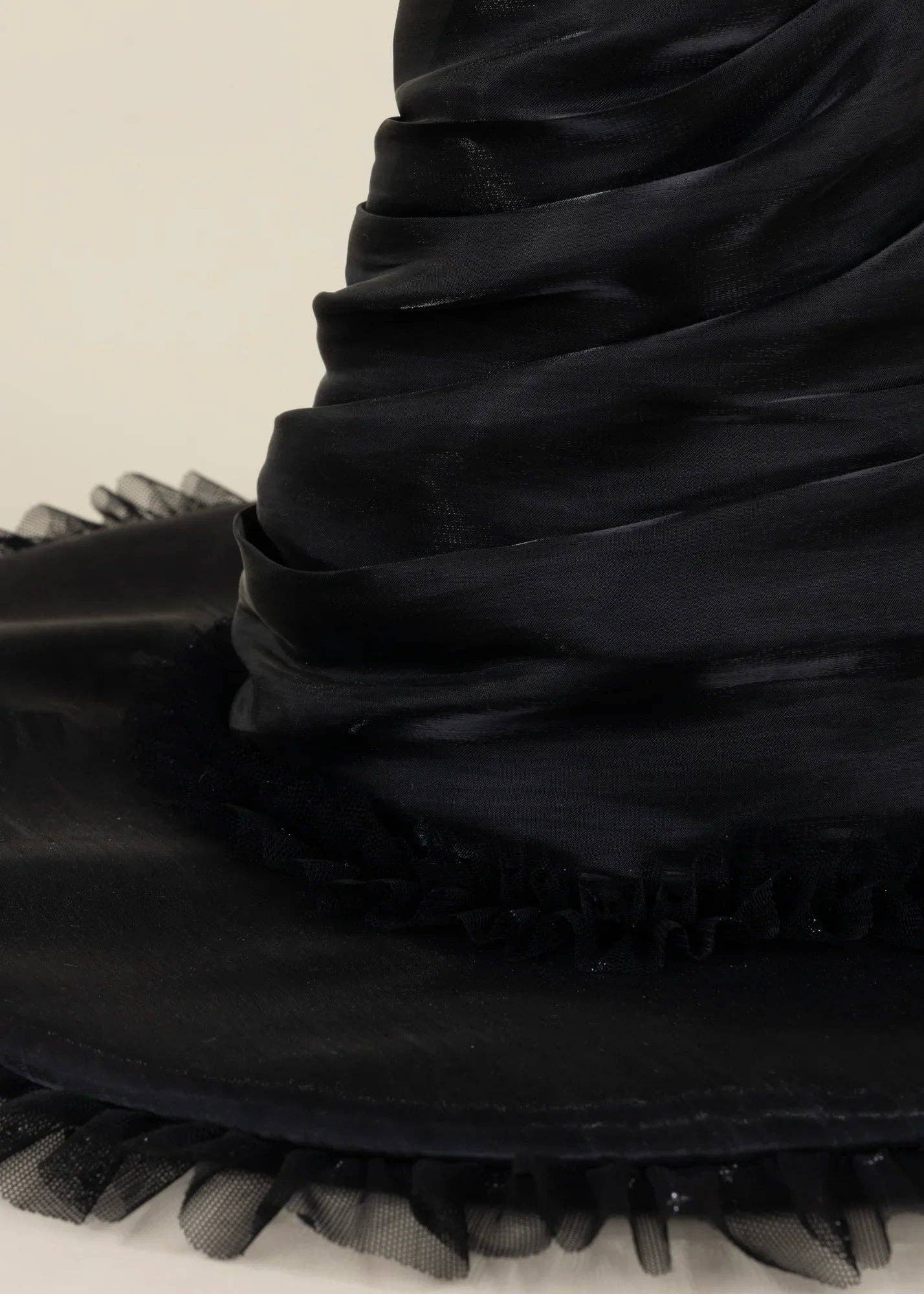 Close-up of a black wide-brimmed hat with gathered fabric and sheer ruffled trim on a light background.