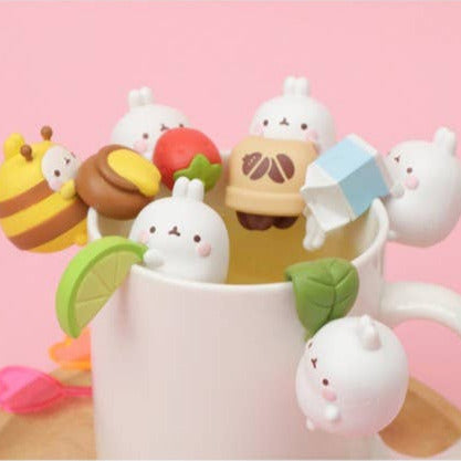 Cute character figurines around a mug on a pink background