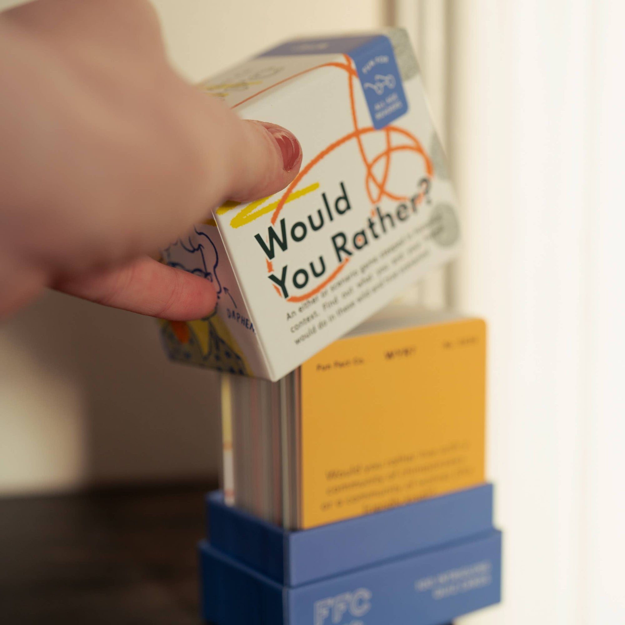 Hand holding a 'Would You Rather?' game box with a blurred background
