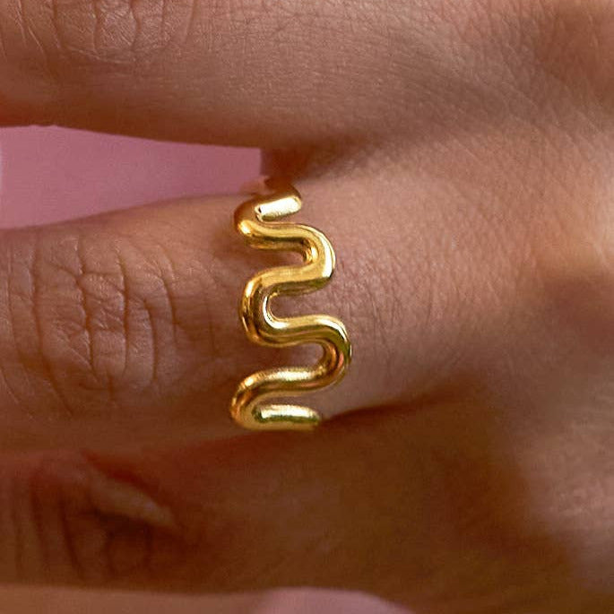 Gold spiral earring on a finger against a pink background
