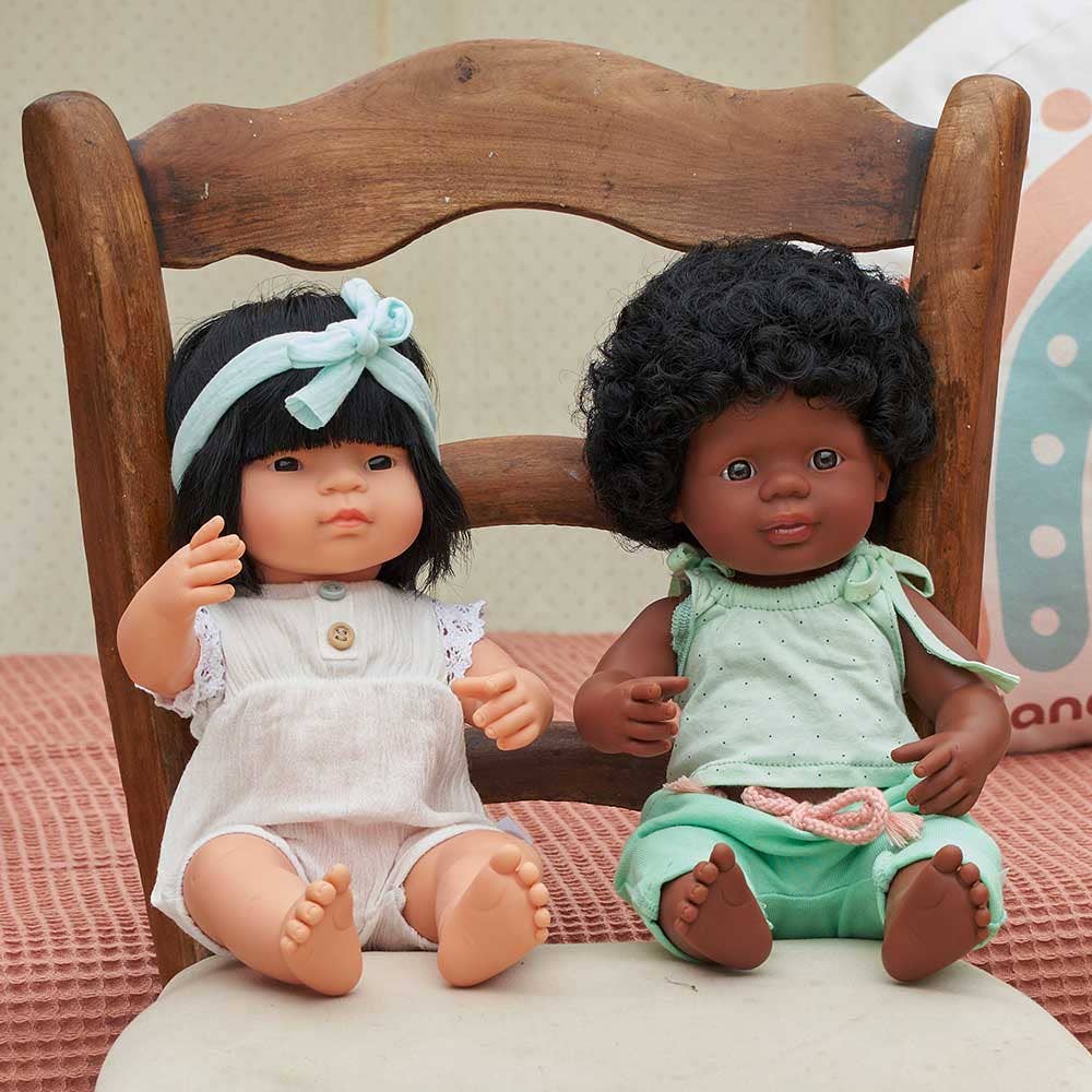 Two dolls sitting on a wooden chair with a soft pink background