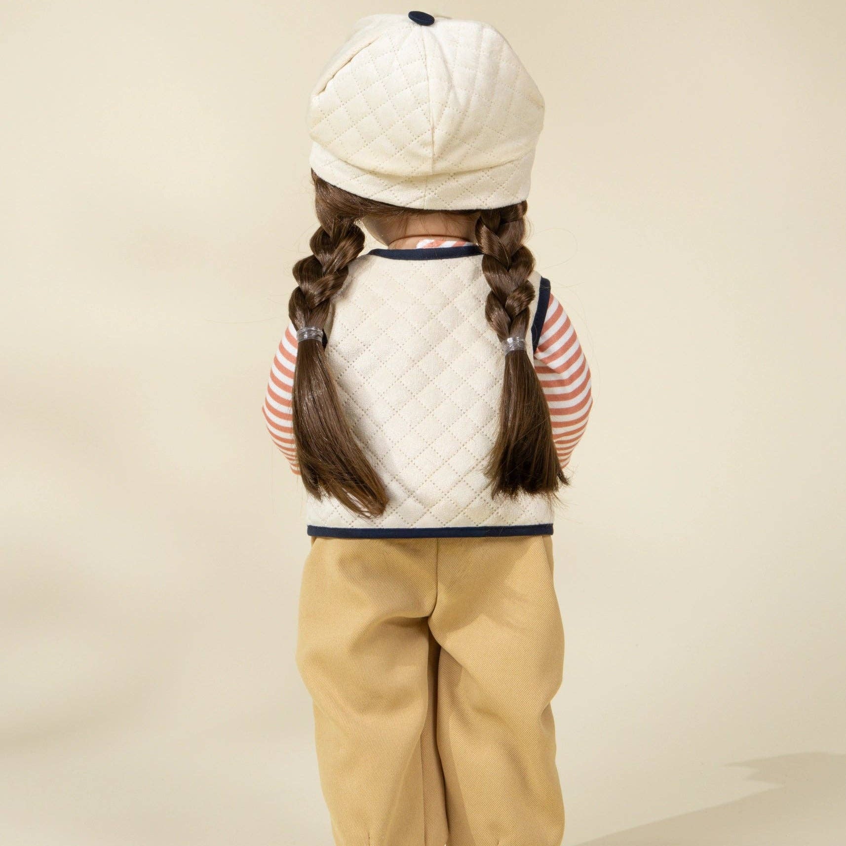 Child wearing a white quilted jacket, beige pants, and a white cap on a beige background