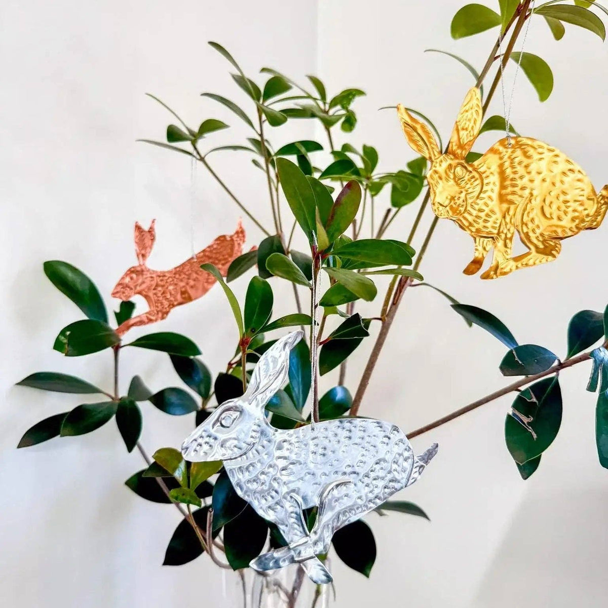 Decorative bunny figurines in a clear vase with green leaves on a white background
