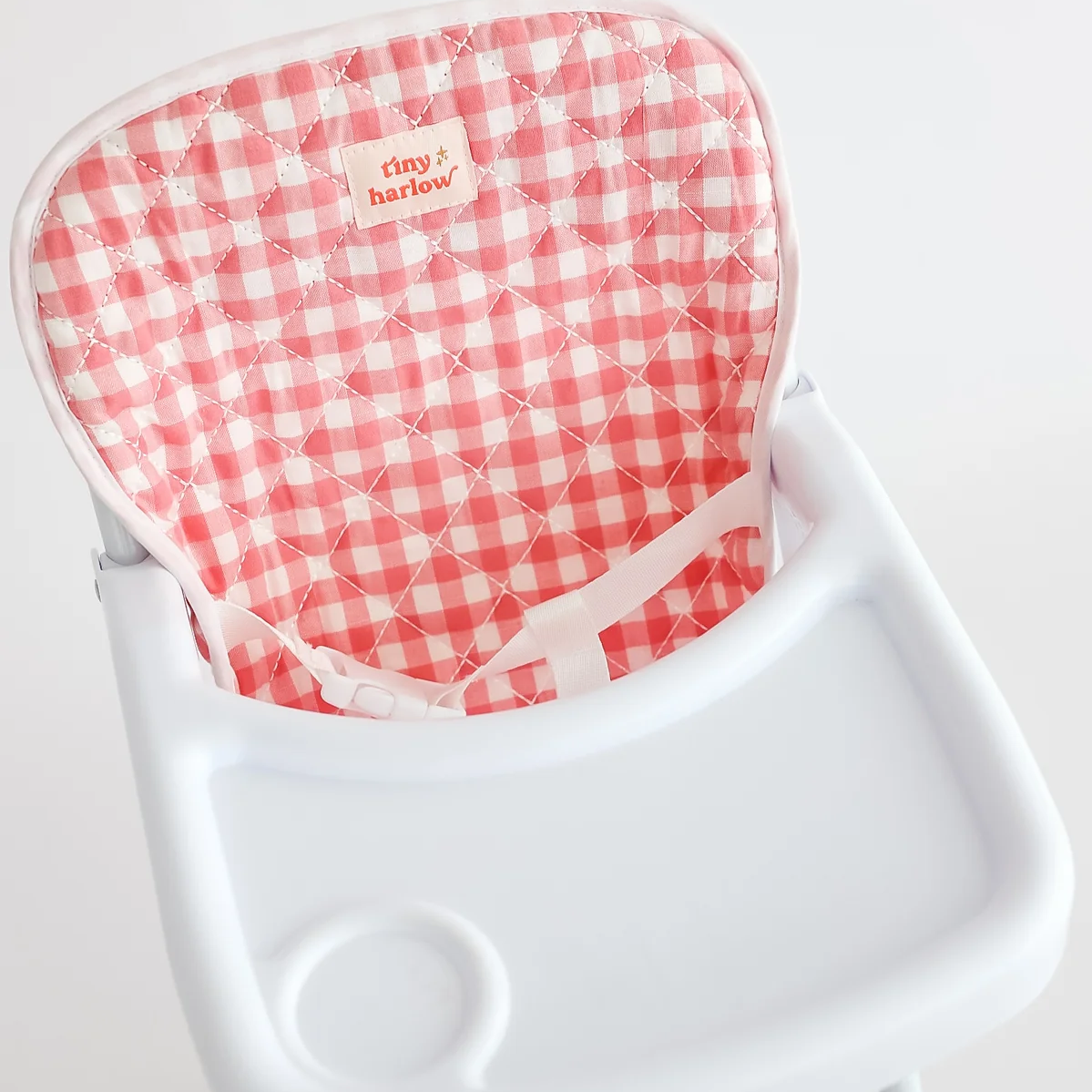 Red and white checkered cushion on a white chair with 'Tiny Harlow' branding.
