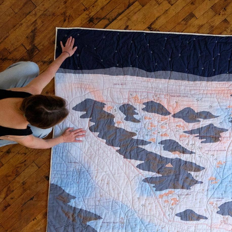 Person arranging a large quilt with bear designs on a wooden floor
