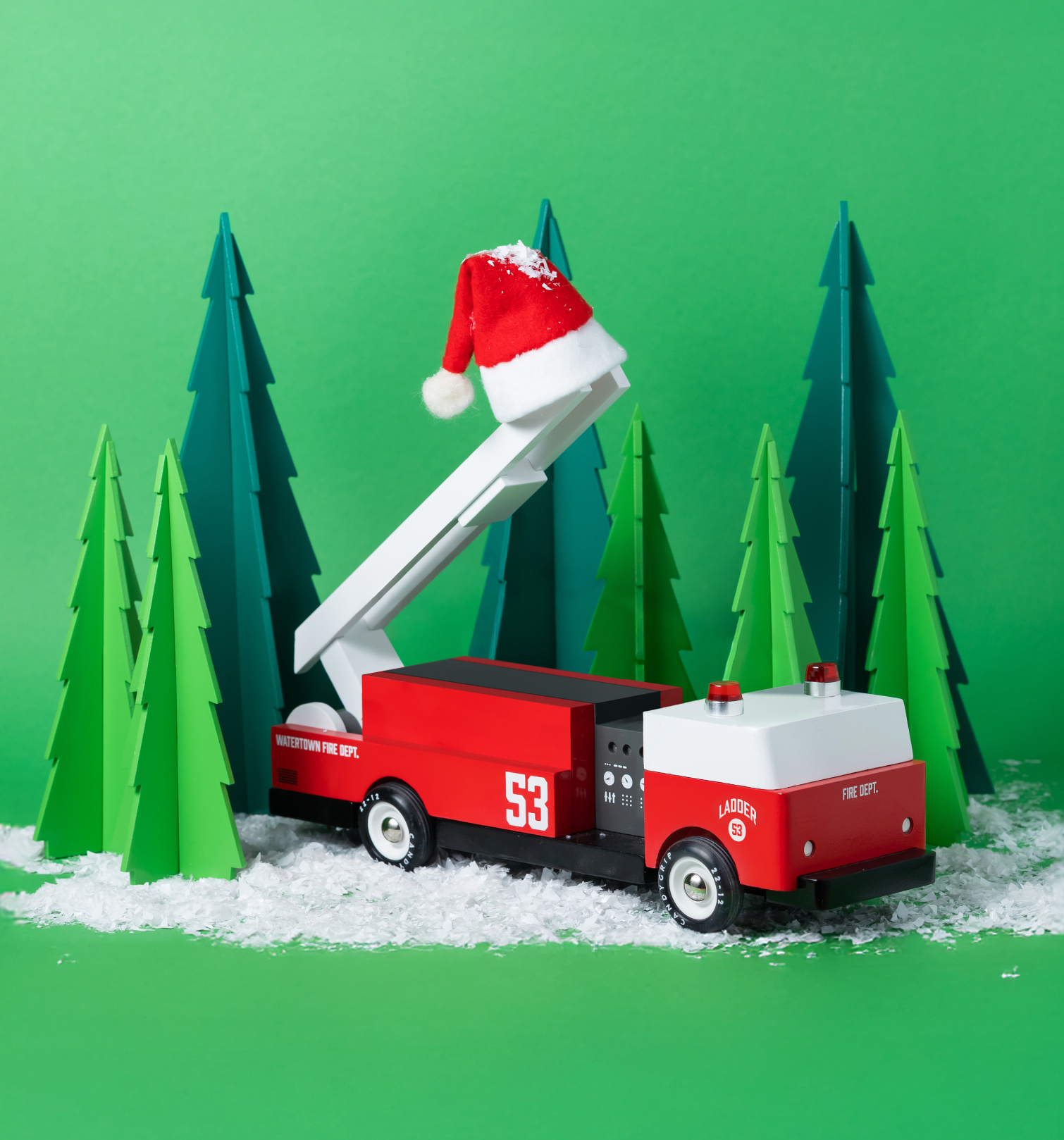 Toy fire truck with a Santa hat on a green background with pine trees