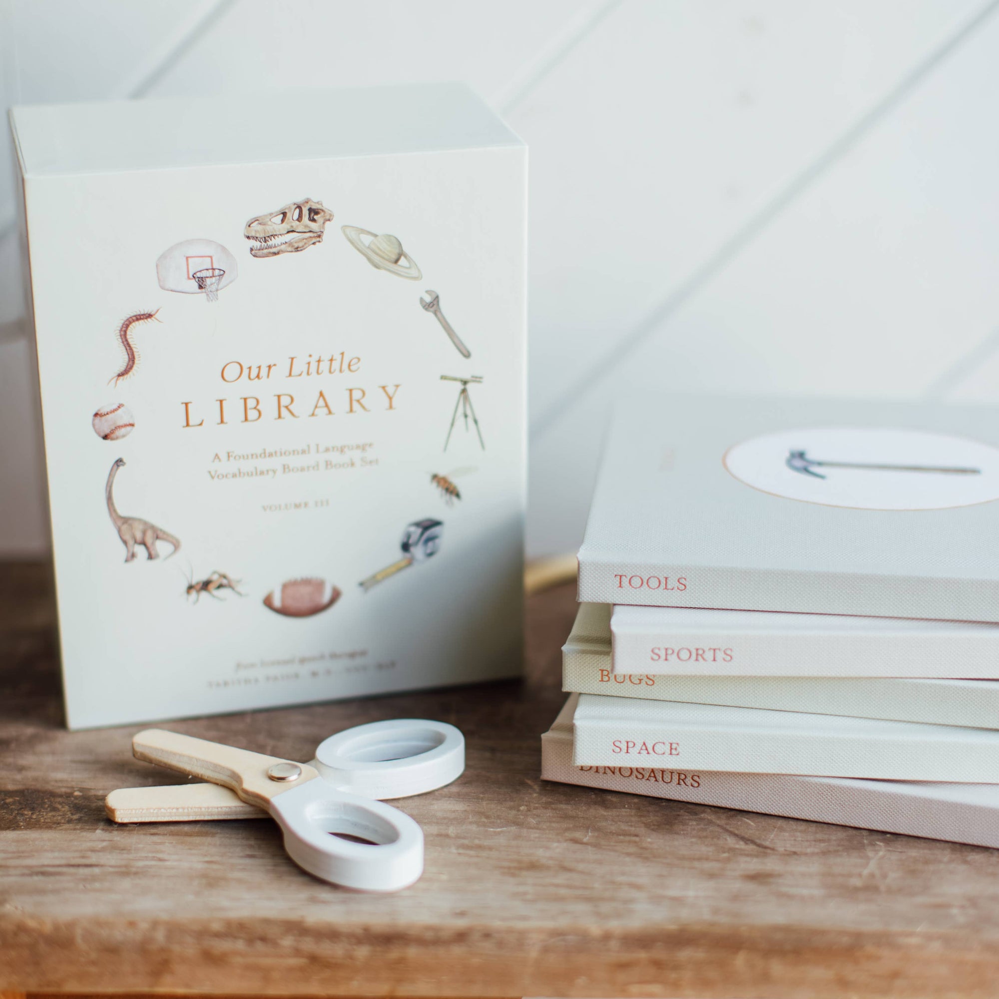 Stack of books titled 'Our Little Library' on a wooden surface with a white background