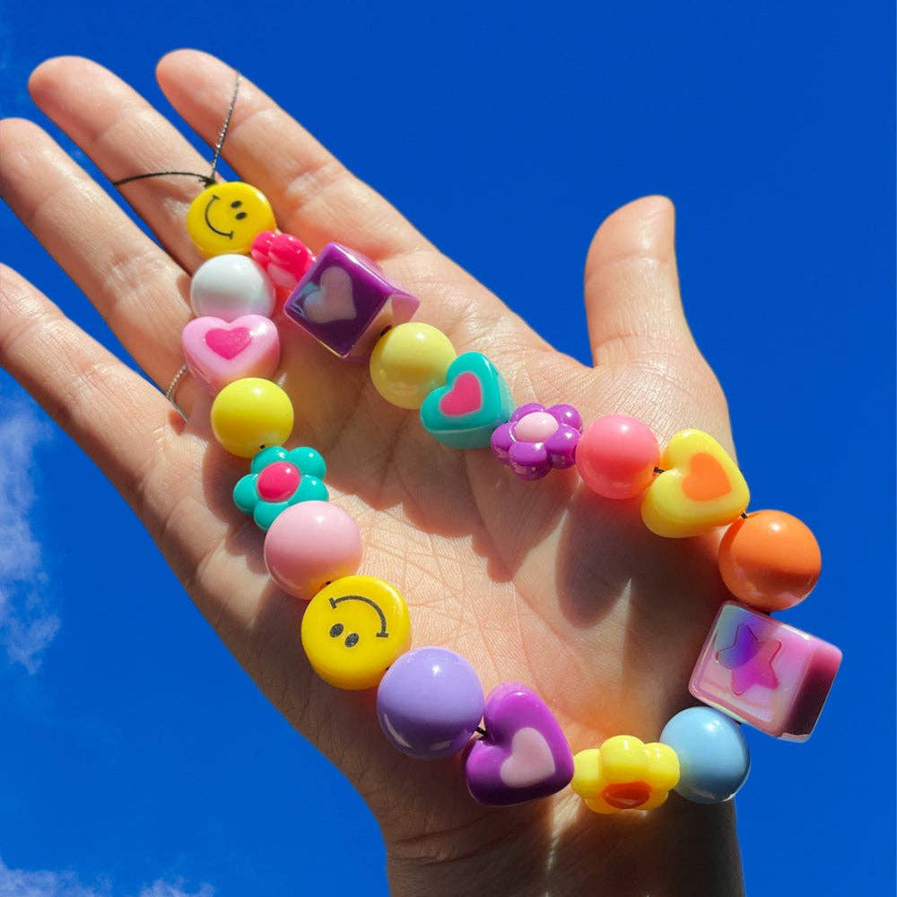 Colorful beaded bracelet with various shapes and patterns held against a blue sky.