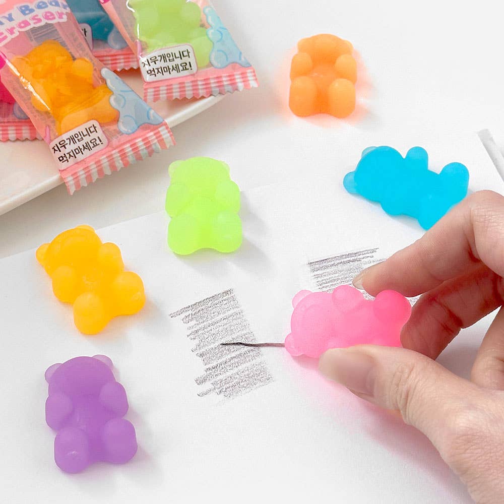 Colorful gummy bear-shaped erasers on a white surface with a hand holding one.