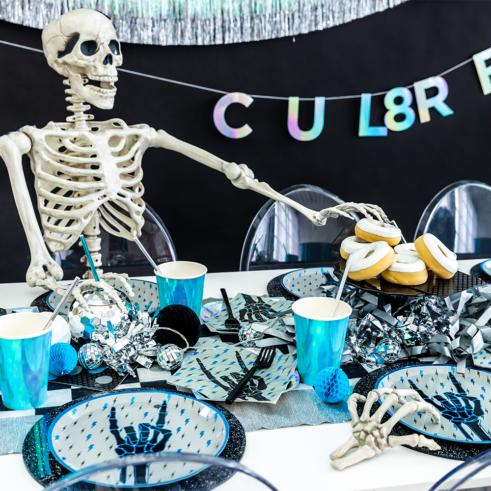Skeleton at a party table with Halloween-themed decorations and 'CU L8R' banner.