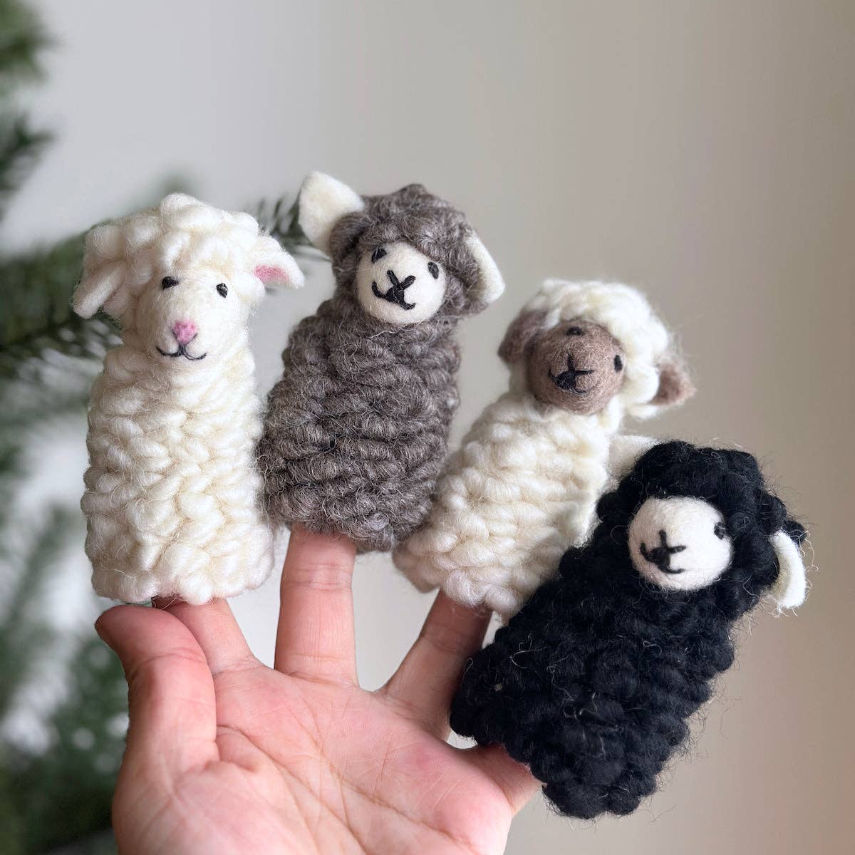 Four crocheted sheep finger puppets held against a blurred natural background