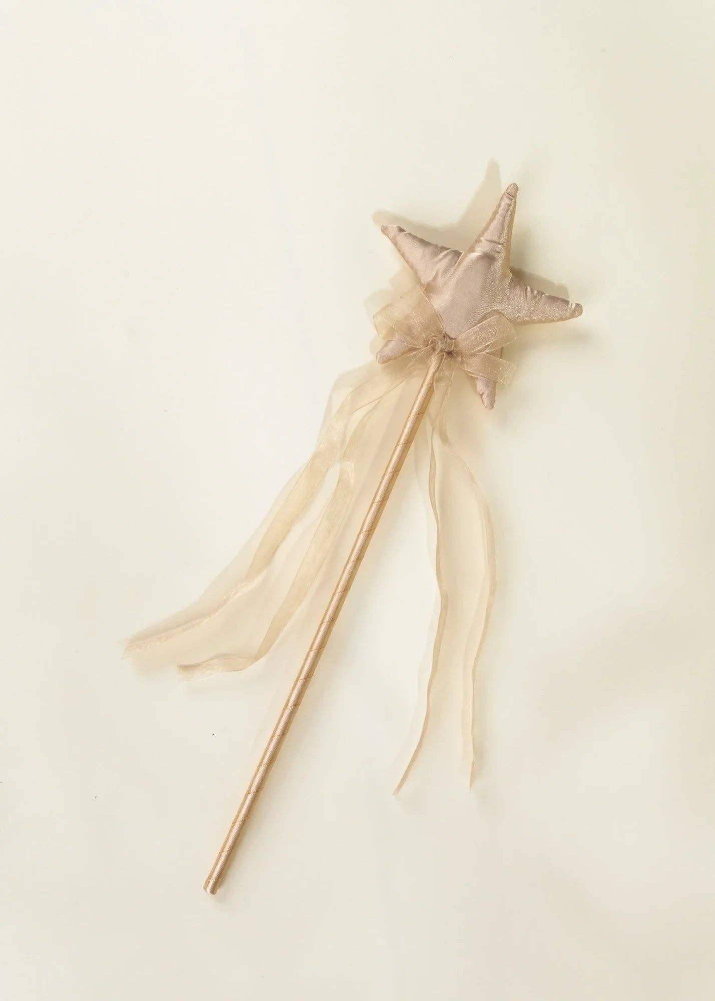 A whimsical star wand with a soft beige fabric star head, sheer tulle ribbon, and a long wooden handle, photographed on a plain cream background.