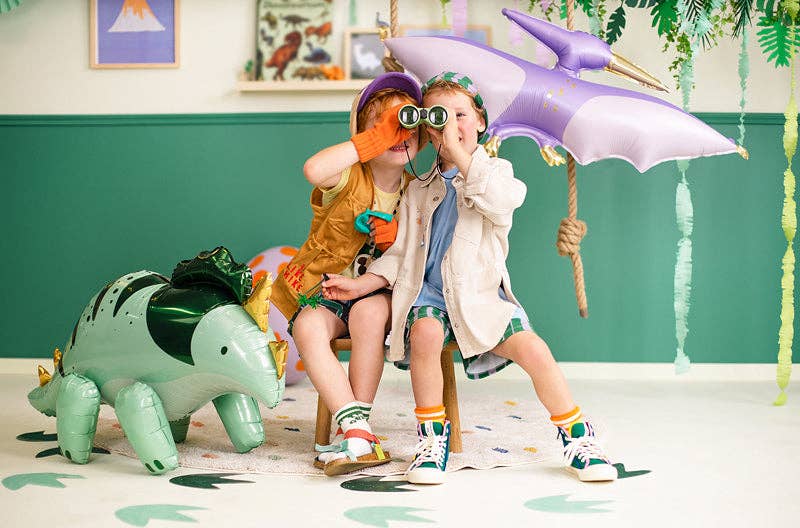 Two children playing with dinosaur toys in a room with a green wall and colorful decorations.