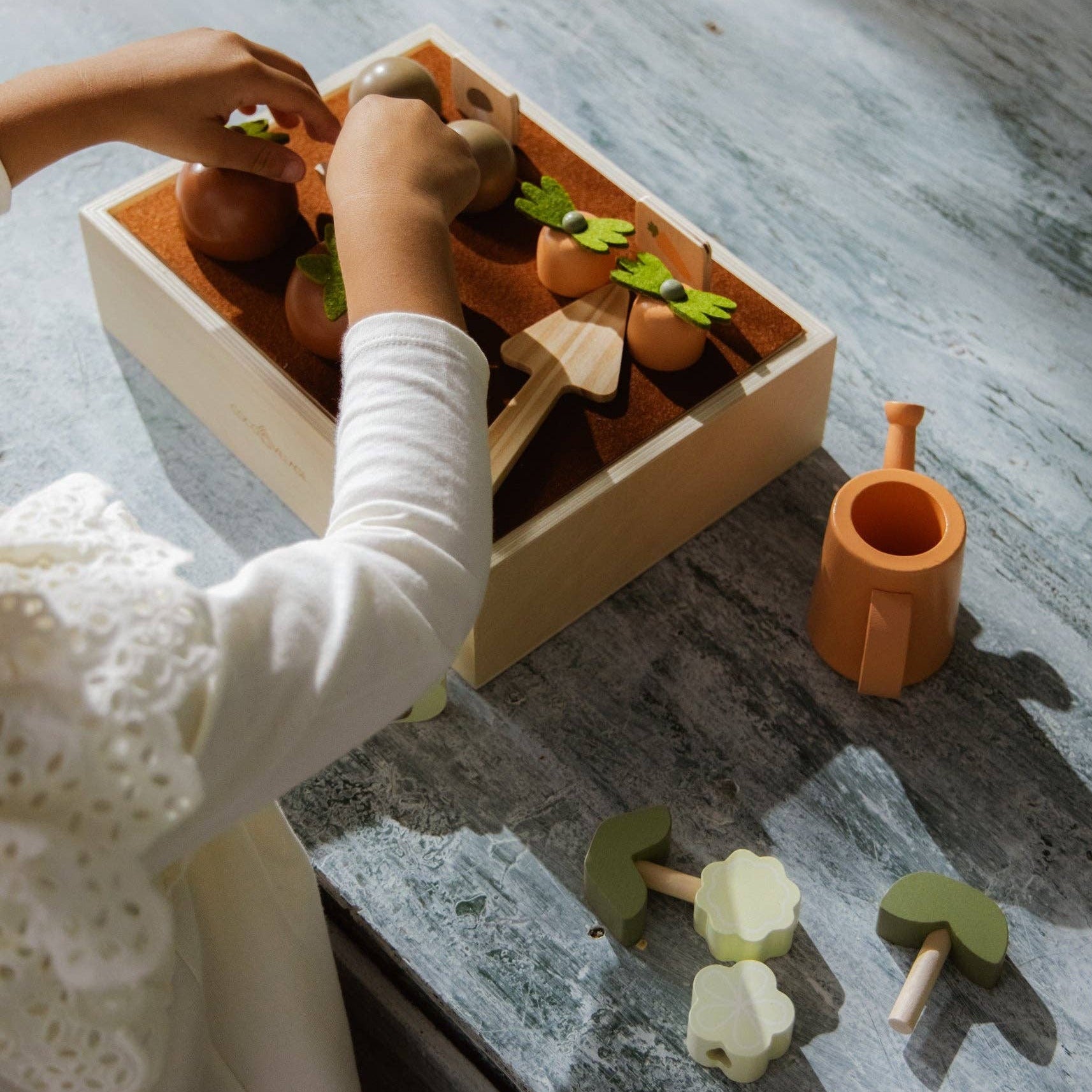 Child playing with wooden gardening toys on a wooden surface