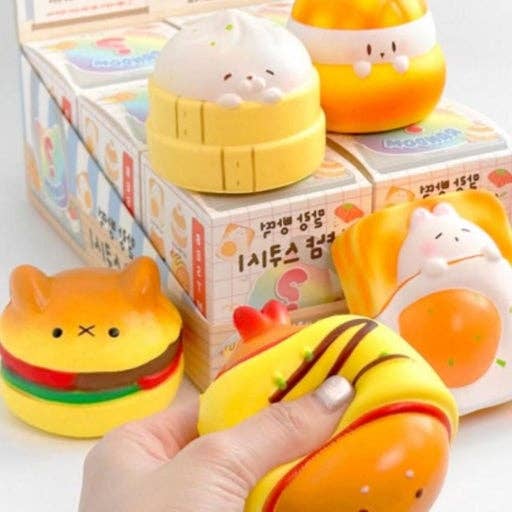 Kawaii-themed squishies with a hand holding one, set against a colorful box background.