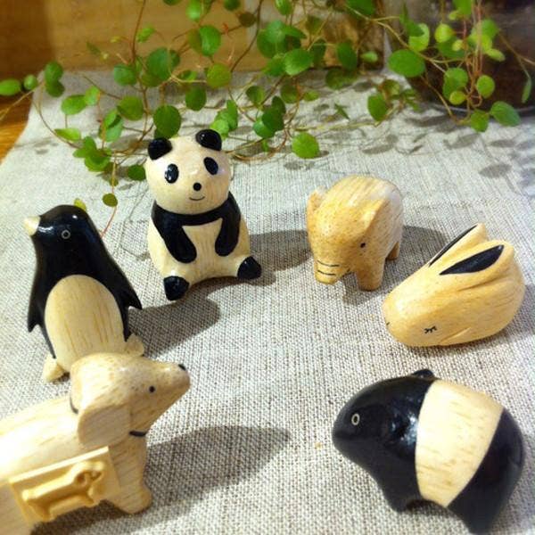 Set of wooden animal figurines on a textured surface with greenery in the background