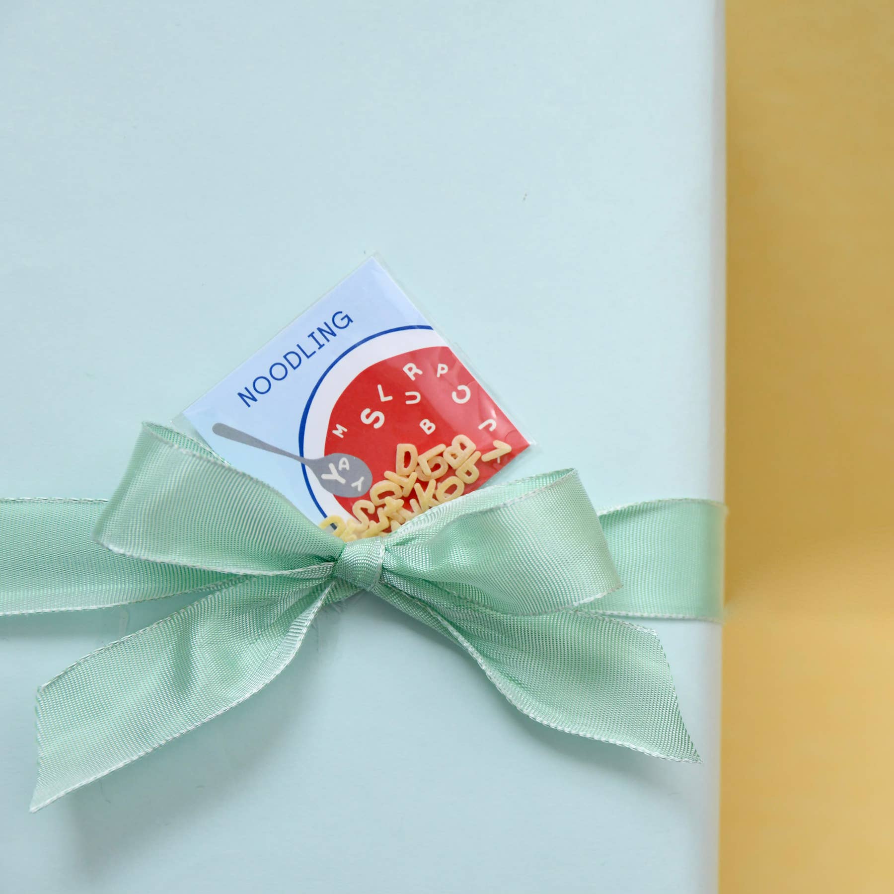 Green ribbon with a noodling-themed card on a light blue and yellow background