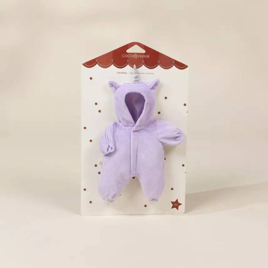 A small lavender plush toy or wearable plush piece with a hood and long sleeves, attached to a white retail card with a red scalloped top and star details, photographed against a warm off-white background.