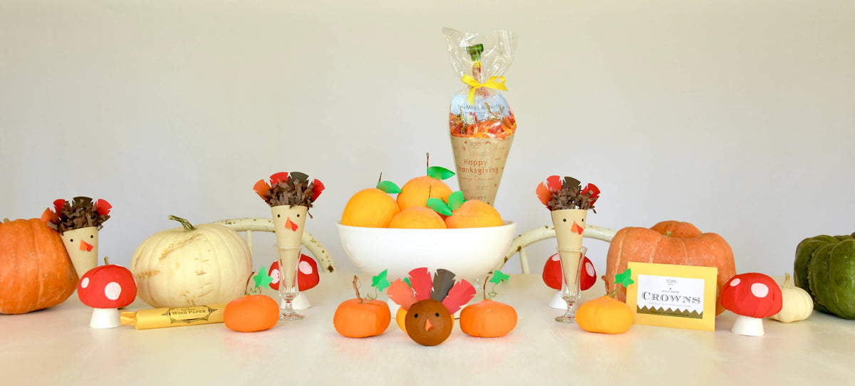 Decorative setup with pumpkins, apples, and a bowl of oranges on a white surface.