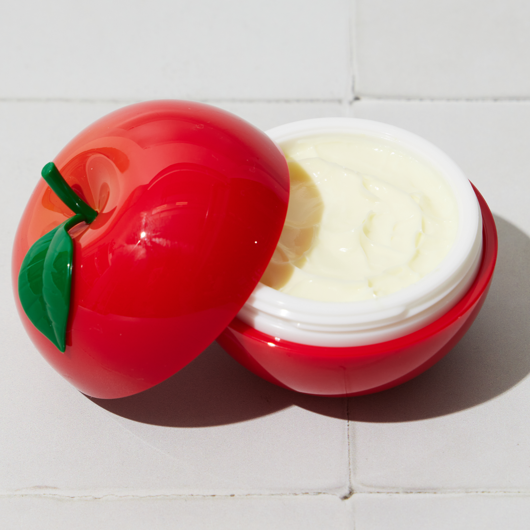 Red apple-shaped container with white cream inside on a light gray background