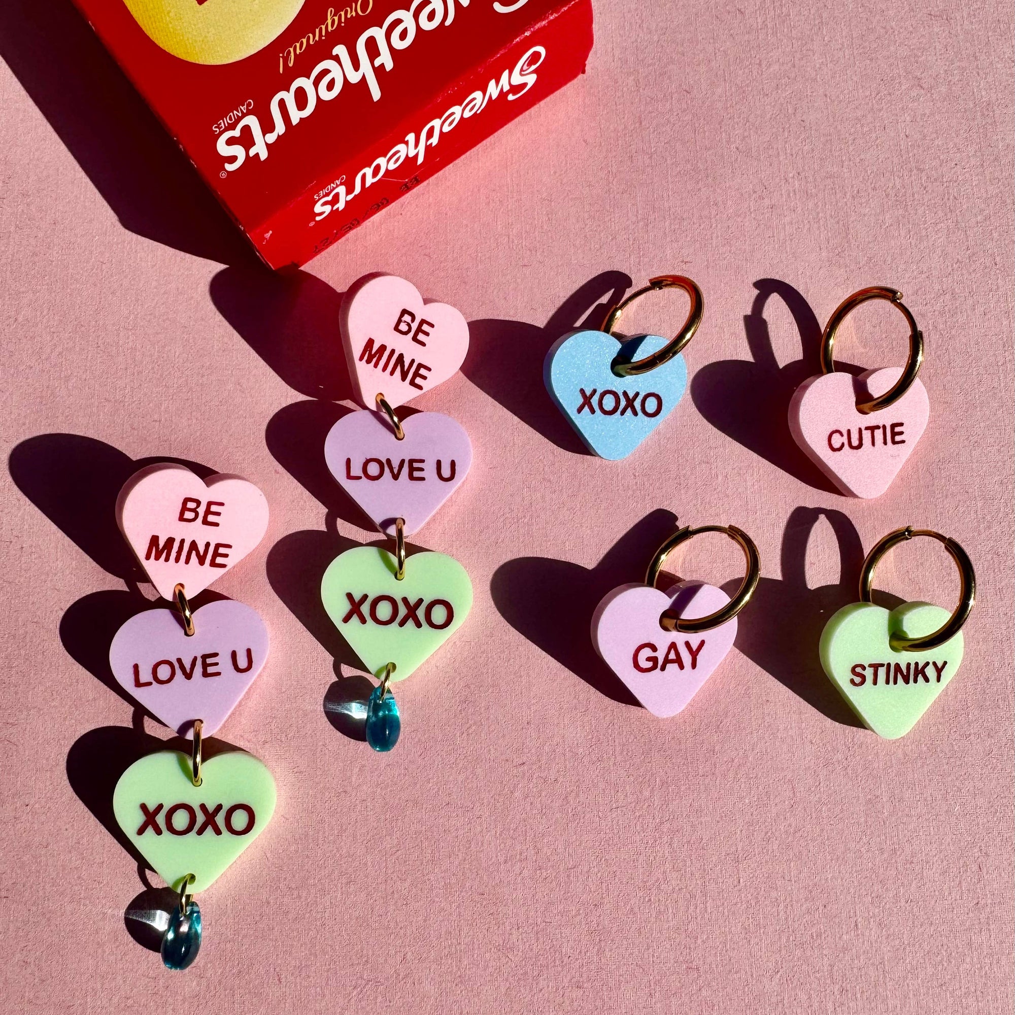 Heart-shaped candy charms with messages next to a SweeTarts box on a pink background