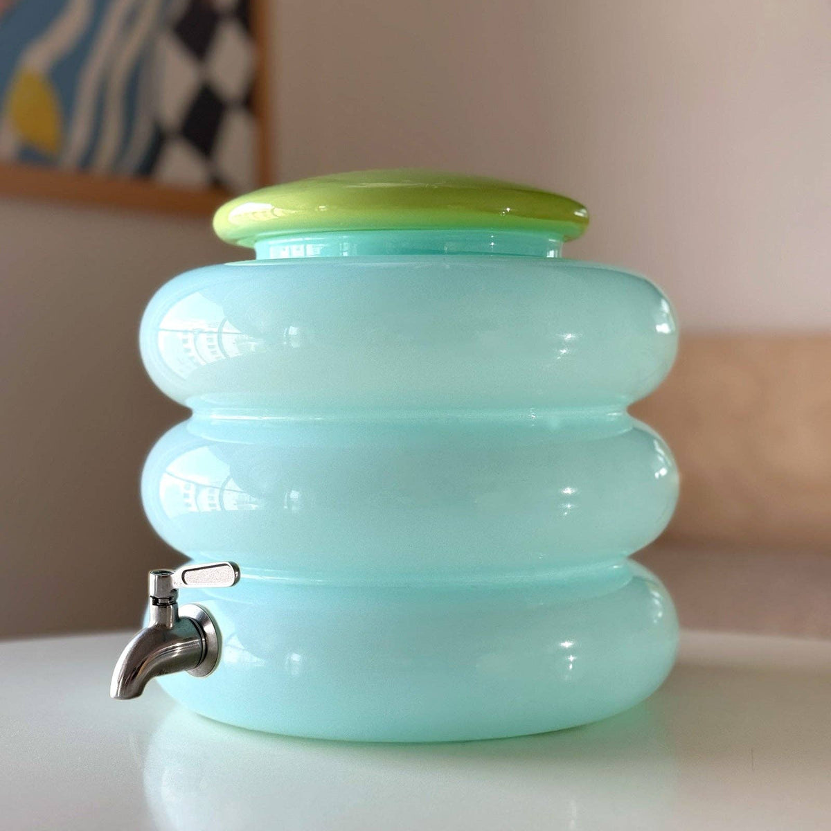 Light blue container with a green lid and silver faucet on a white surface.